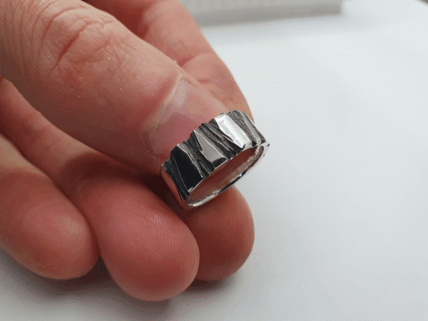 oxidised-silver-ring-fractur-held-distance shiny silver ring with deep black textures – held in hand